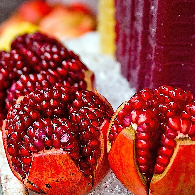 Pomegranate cut open to reveal red seeds on a white surface.